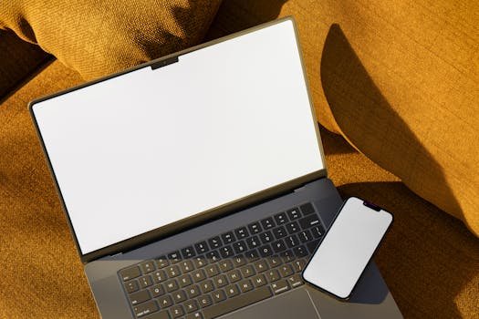 Top view of laptop and smartphone with blank screens on a comfortable sofa in warm light.